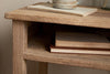 A close-up of the Iya Reclaimed Wood Bedside Table by nkuku, featuring a chunky natural structure with a ceramic mug and closed book on top, and two vintage books stacked on the lower shelf.
