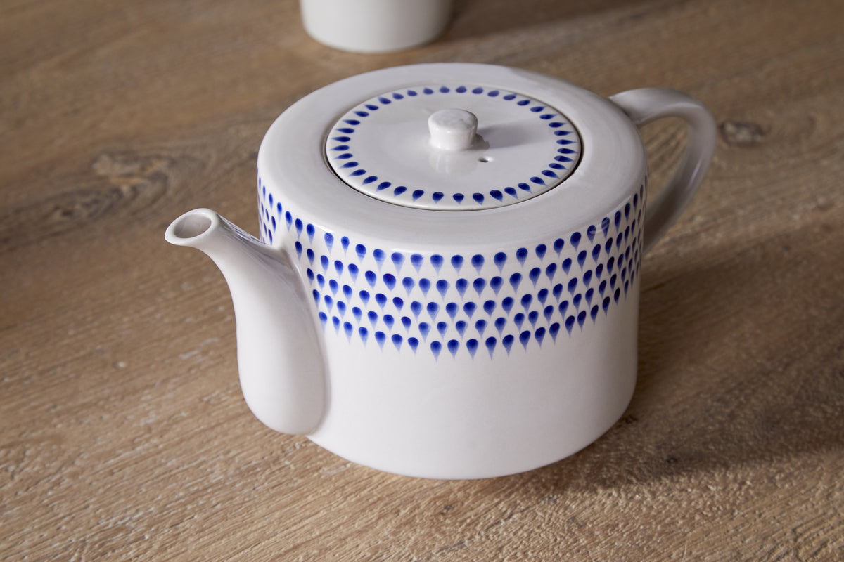 The Indigo Drop 4 Person Teapot by nkuku features hand-painted cream ceramic with indigo blue dots, a short spout, and round lid—making it a charming gift for tea lovers.