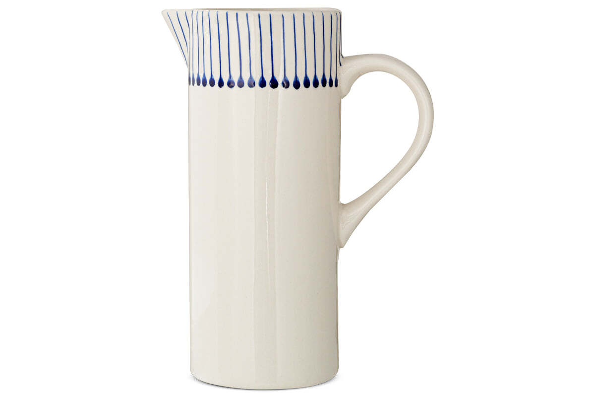 The Iba Jug - Indigo by nkuku is a tall, white ceramic pitcher featuring artisanal craftsmanship, a curved handle, narrow spout, and thin indigo lines near the rim for a modern touch.