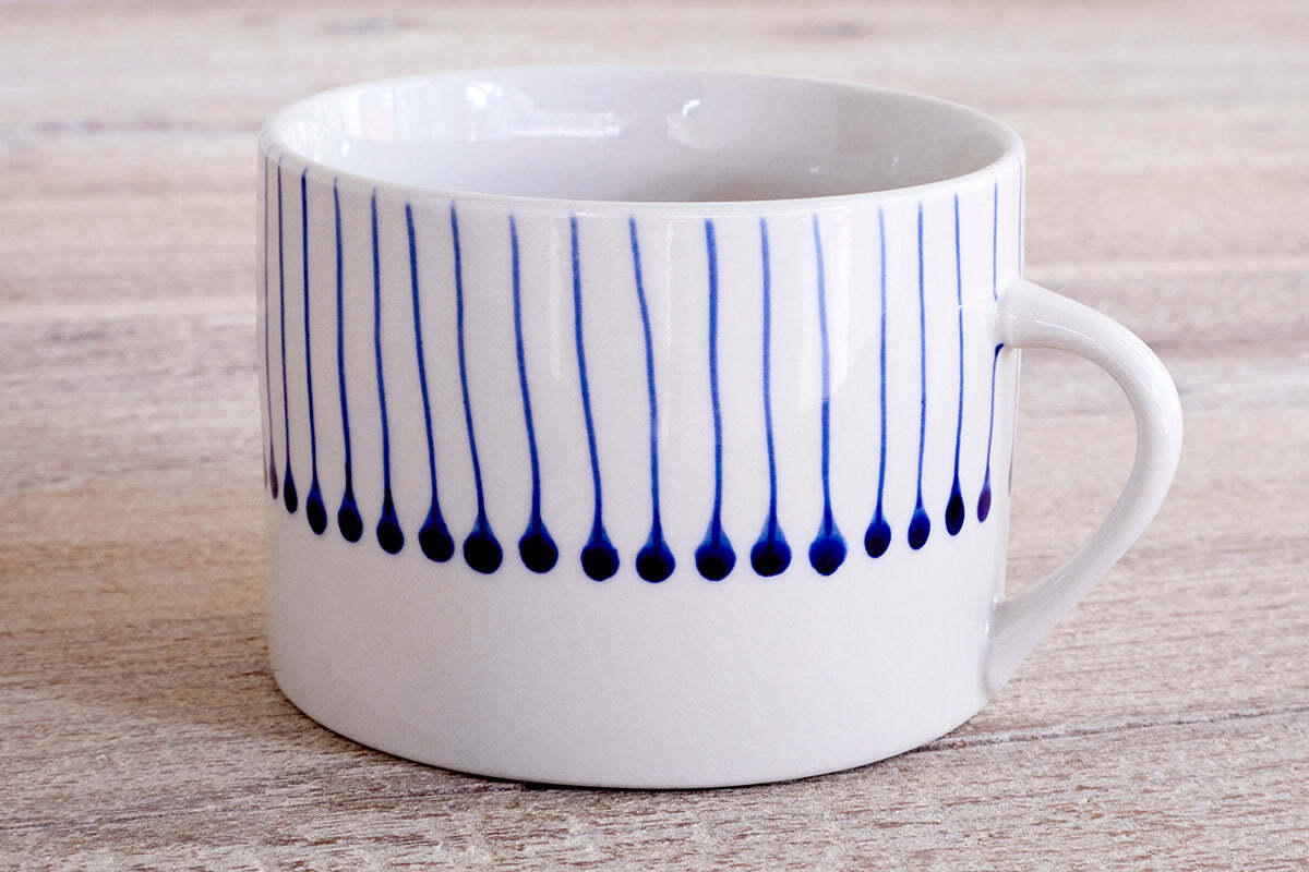 The nkuku Iba Mug - Indigo - Large (Set of 2) features a white ceramic body with simple handles and vertical blue lines ending in dots, inspired by Iba design, spaced around the upper half. Perfect for modern coffee moments.