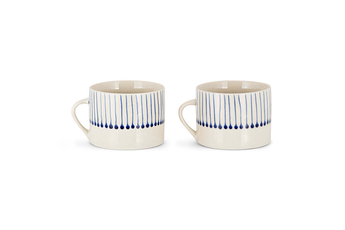 The nkuku Iba Mug - Indigo - Large (Set of 2) features hand-painted, cream-colored ceramics with vertical blue lines and dots on the upper half, showcasing a simple modern design. Both mugs have handles and are displayed against a plain white background.