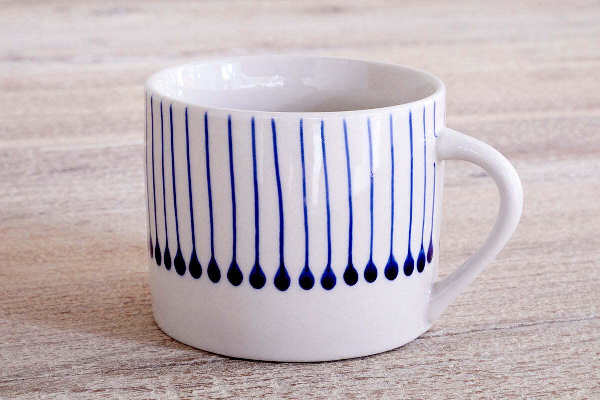 The nkuku Iba Mug - Indigo - Small (Set of 2) features a white ceramic design with a simple handle and hand-painted vertical blue teardrop lines—ideal for fans of unique, artisanal coffee cups.