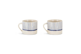 The nkuku Iba Mug - Indigo - Small (Set of 2) features white ceramic mugs with handles, decorated with vertical blue lines and indigo drop shapes for a modern, hand-painted look. Both are shown side by side on a white background.