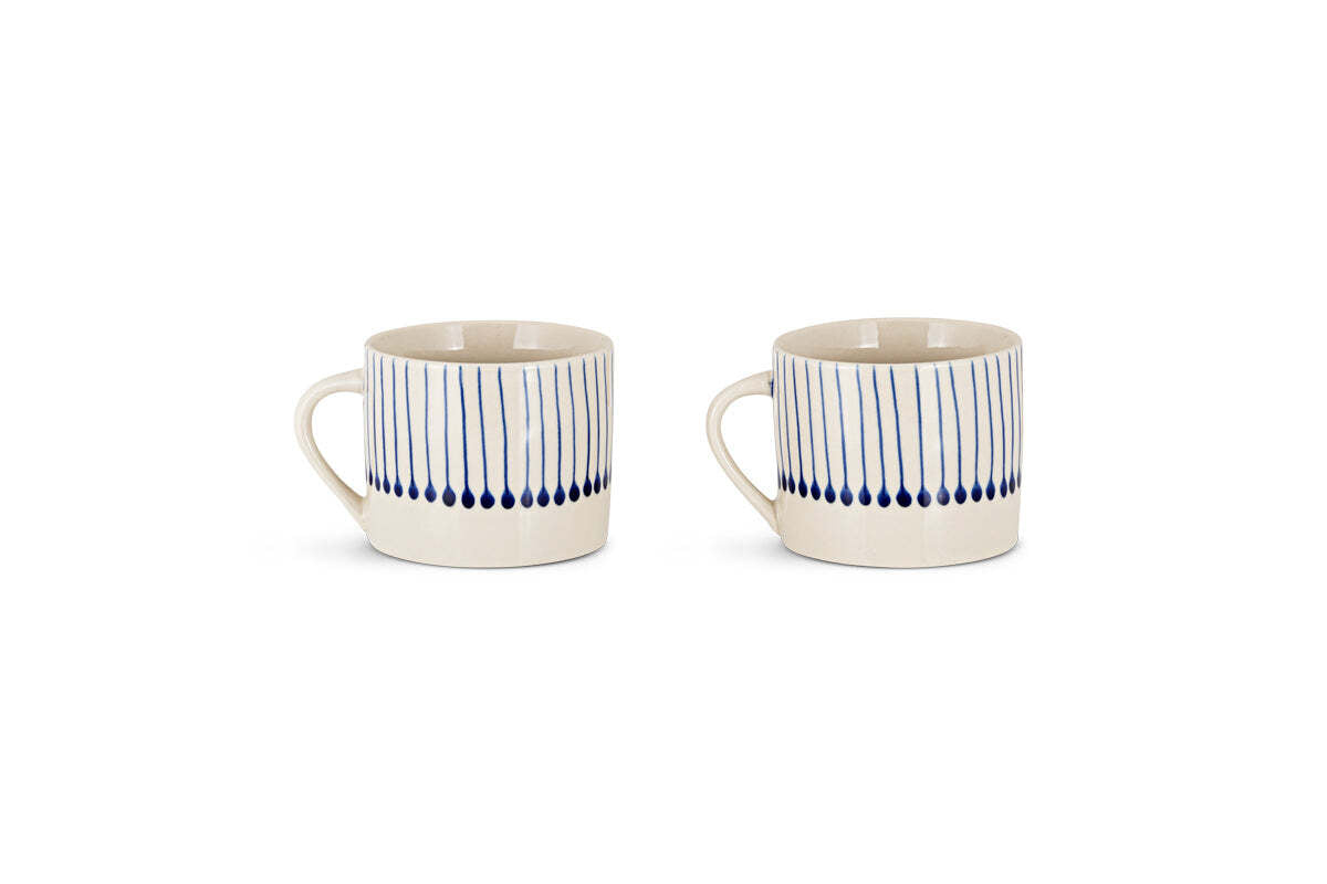 The nkuku Iba Mug - Indigo - Small (Set of 2) features white ceramic mugs with handles, decorated with vertical blue lines and indigo drop shapes for a modern, hand-painted look. Both are shown side by side on a white background.