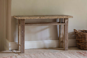 The nkuku Ibo Reclaimed Wood Console Table – Natural stands against a light beige wall, radiating rustic charm. A wicker basket sits to its right.