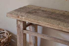 A close-up, low-angle shot of the nkuku Ibo Reclaimed Wood Console Table - Natural radiates rustic charm, showcasing its textured reclaimed wood surface with weathered grain and visible nail holes.