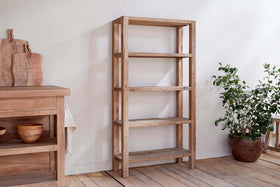 The Ibo Reclaimed Wood Shelf – Natural – Wide by nkuku, with five shelves, stands on a wooden floor beside a potted plant, adding rustic charm to your space.