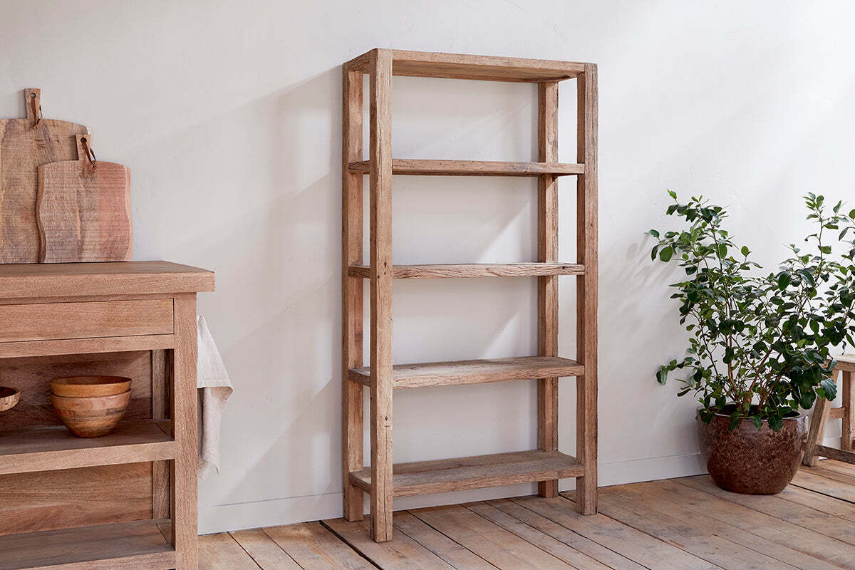 The Ibo Reclaimed Wood Shelf – Natural – Wide by nkuku, with five shelves, stands on a wooden floor beside a potted plant, adding rustic charm to your space.