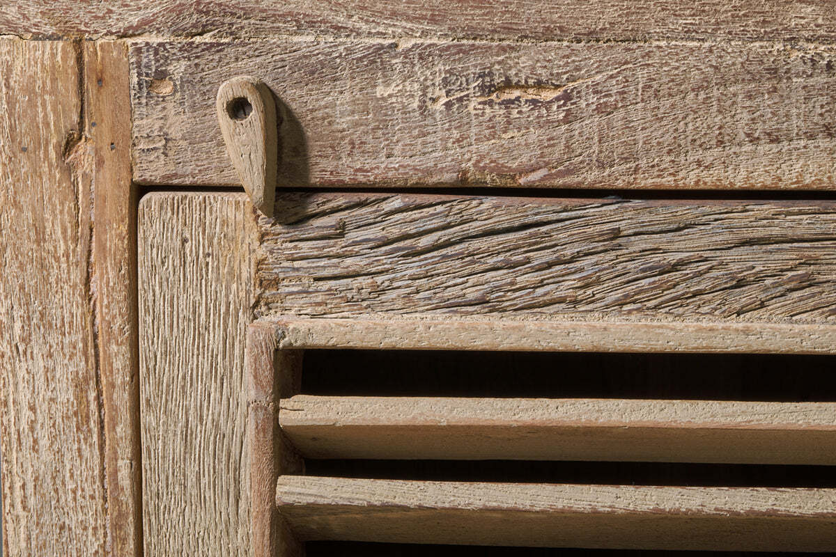 Close-up of the Ibo Reclaimed Wooden Slatted Cabinet – Natural - Small by nkuku, showing weathered horizontal slats, textured wood grain, and a metal hinge that highlights rustic Indian artisan craftsmanship.