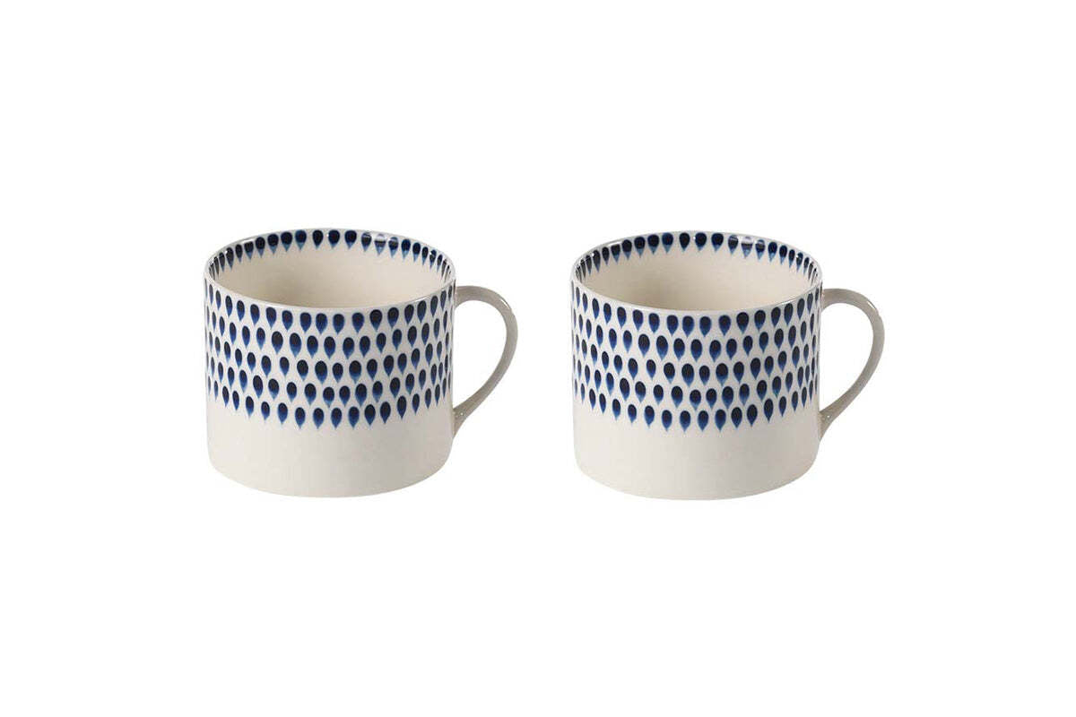 The nkuku Indigo Drop Mug - Cream & Indigo - Large (Set of 2) features two large white ceramic mugs with handles, each adorned near the rim with indigo teardrop motifs that wrap around the top half against a plain background.