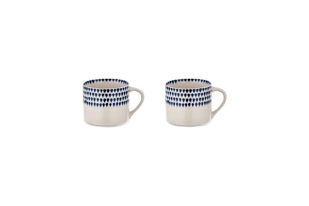 The nkuku Indigo Drop Mug - Cream & Indigo - Small (Set of 2) features two cream mugs with handles and hand-painted indigo drop designs around the top, displayed side by side on a plain white background.