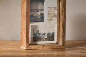 The Indu Standing Mango Wood Frame - Natural by nkuku, crafted from rustic-finished mango wood, displays two vintage black-and-white outdoor photos and text. It stands on a wooden surface against a plain, light-colored wall for added charm.
