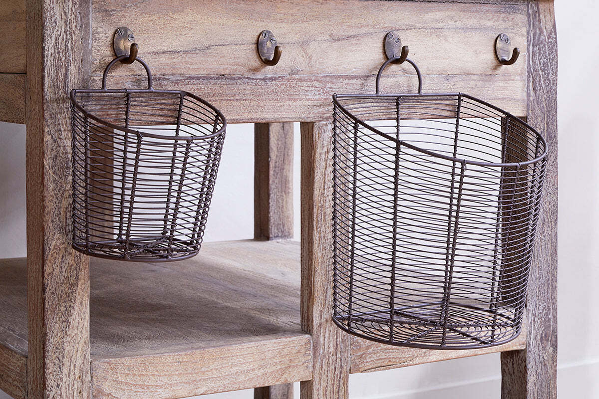 Two oval Inkollu Wall Hung Baskets (set of 2) by nkuku, in aged brass, are hung from hooks on a rustic wooden table with a naturally weathered finish and a lower shelf.