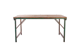 The Ishan Reclaimed Folding Dining & Coffee Table by nkuku features a rectangular metal frame with a worn wooden top, green-painted, slightly rusted legs, and sturdy crossbars, shown against a plain white background.