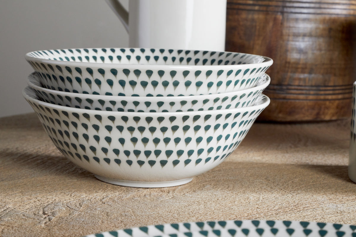 Three stacked nkuku Juniper Drop Cereal Bowls in Cream & Juniper, featuring a green drop pattern, sit on a beige surface among ceramic and wooden pieces—perfect for bringing style to everyday dining.