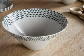 The nkuku Juniper Drop Serving Bowl - Cream & Juniper - Large features a white, cone-shaped ceramic design with small dark blue teardrop patterns around the rim, making it an elegant centrepiece on any table.
