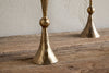 Close-up of two nkuku Javanee Candle Holders in Antique Brass, featuring hammered texture on a rustic wooden surface against a light textured wall, highlighting their sculptural elegance.
