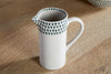 The nkuku Juniper Drop Jug - Cream & Juniper - Small features a white ceramic design with a handle, spout, and blue-green teardrop motifs—ideal for modern tableware collections.