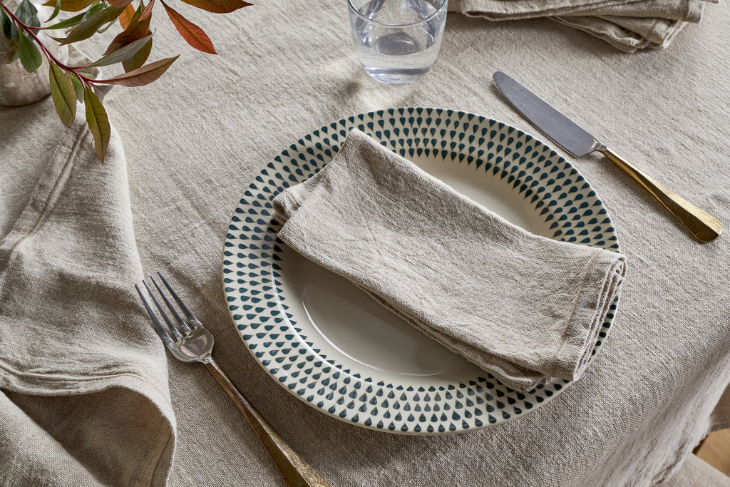 A plate with a fork rests on the table, complemented by nkukus Junto Linen Napkin - Natural (Set of 4), creating a refined dining setting.