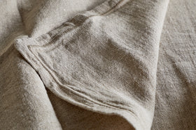 Close-up of the nkuku Junto Linen Napkin - Natural (Set of 4): beige, textured linen with visible folds and seams, highlighting its natural weave—perfect for a neutral table setting.
