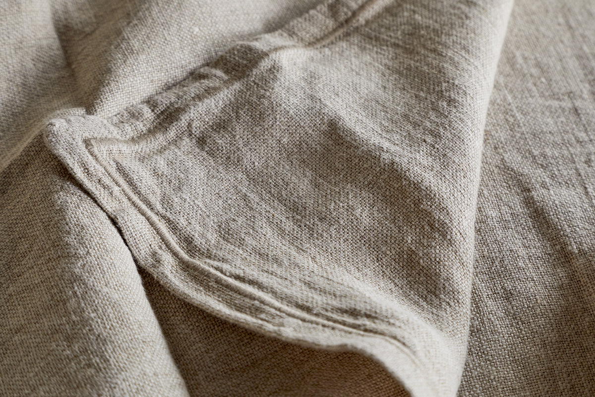 Close-up of the nkuku Junto Linen Napkin - Natural (Set of 4): beige, textured linen with visible folds and seams, highlighting its natural weave—perfect for a neutral table setting.