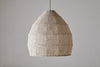 The nkuku Jahari Woven Jute Pendant - Natural hangs from the ceiling against a plain, light gray wall, offering rustic charm with its woven beige dome-shaped design.