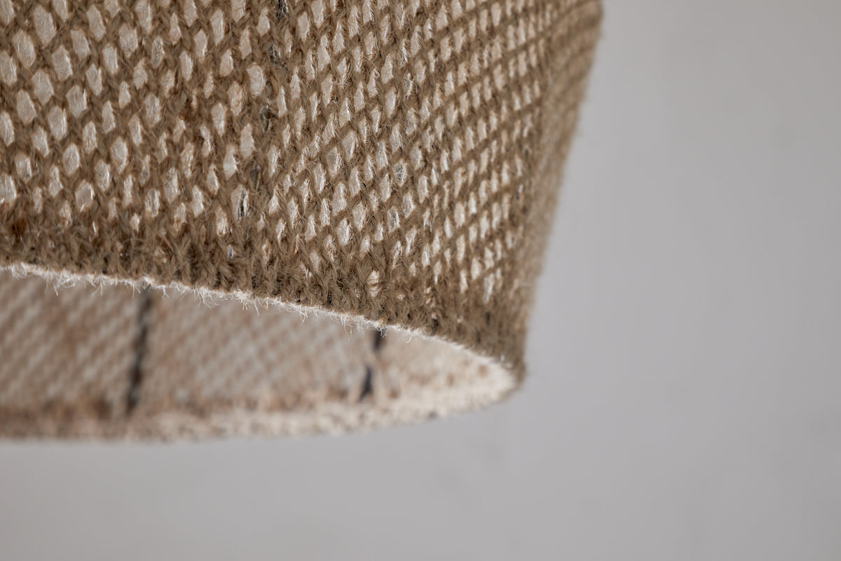 Close-up of the nkuku Jahari Woven Jute Pendant in Natural, featuring light brown jute fibers with a textured, mesh-like pattern against a plain light gray background—ideal for rustic home decor.