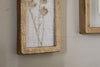 A close-up of nkuku’s Jahala Wall Hung Photo Frame in antique brass, showcasing pressed dried flowers on white mesh, hangs on a light wall, with another thick-framed photo frame partially visible to the right.