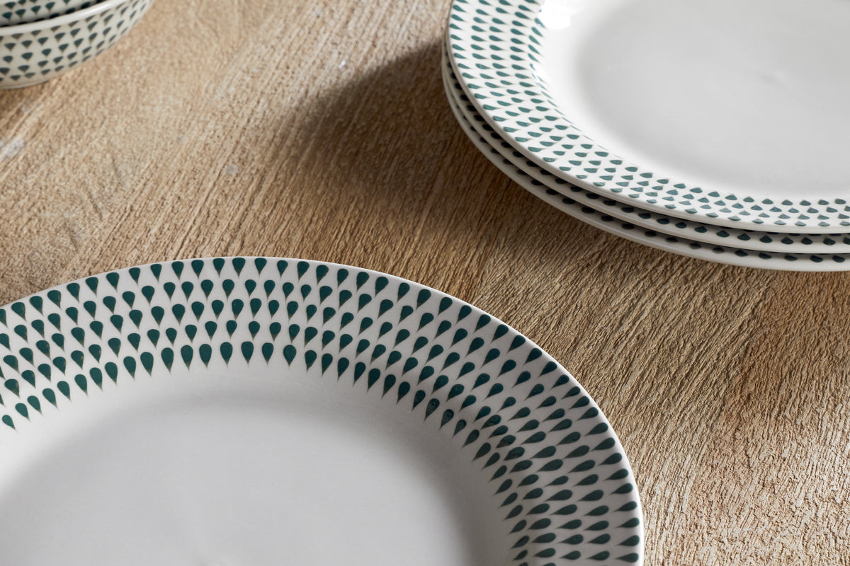 A close-up of nkukus Juniper Drop Dinner Plates in cream & juniper, featuring a green drop pattern along the rim and stacked neatly on a wooden surface.