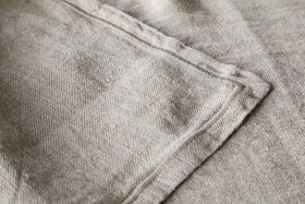 A close-up of the Junto Linen Runner - Natural (Large) by nkuku highlights its beige linen fabric, visible stitching, and neatly sewn seam for a refined, neutral table runner.