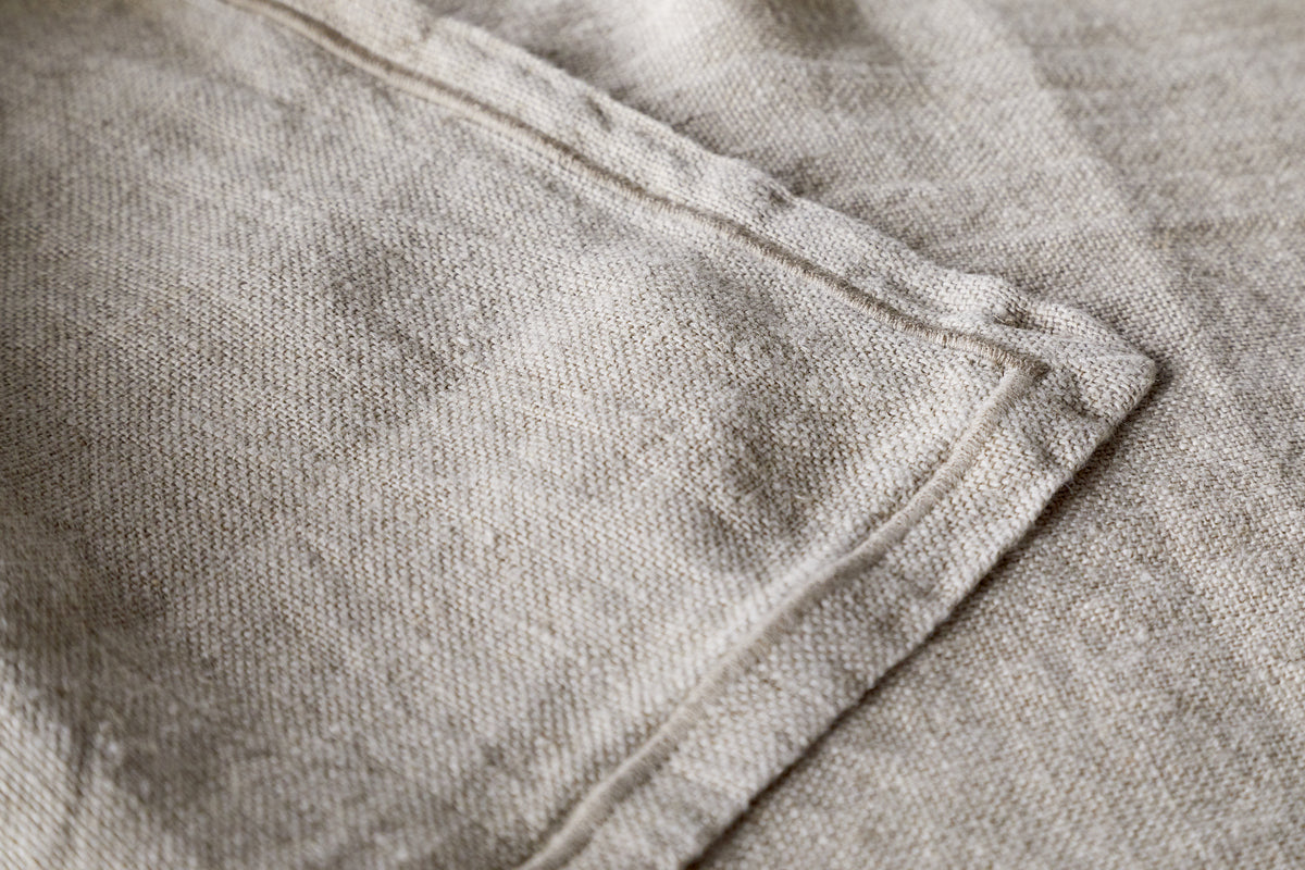 A close-up of the Junto Linen Runner - Natural (Large) by nkuku highlights its beige linen fabric, visible stitching, and neatly sewn seam for a refined, neutral table runner.