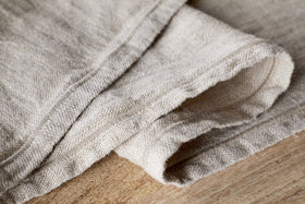 Close-up of the nkuku Junto Linen Runner in Natural (Large), showing its durable texture and visible seams, neatly folded on wood—a versatile neutral table runner for any decor.