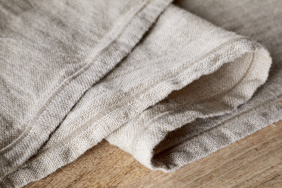 Close-up of the nkuku Junto Linen Runner in Natural (Large), showing its durable texture and visible seams, neatly folded on wood—a versatile neutral table runner for any decor.