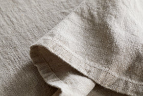 Close-up of the nkuku Junto Linen Tablecloth in Natural (Large), showcasing its beige, textured linen and natural weave—durable and elegant with a neatly folded section for refined table settings.