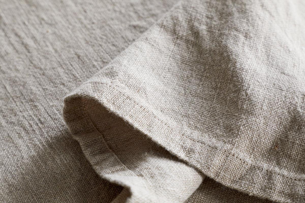 Close-up of the nkuku Junto Linen Tablecloth in Natural (Large), showcasing its beige, textured linen and natural weave—durable and elegant with a neatly folded section for refined table settings.