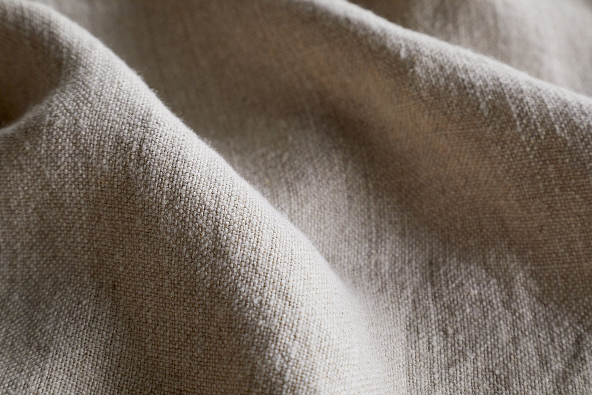 Close-up of the Junto Linen Tablecloth in Natural by nkuku, featuring a beige, textured weave with soft folds and gentle shadows—a versatile, neutral large tablecloth perfect for any setting.