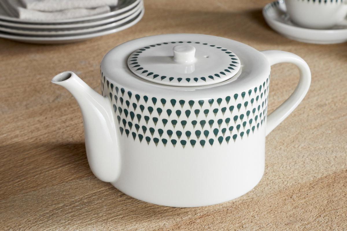 The nkuku Juniper Drop 4 Person Teapot in Cream & Juniper, featuring green teardrop patterns, sits on a wooden table with matching plates and cup—the ideal gift for tea lovers.