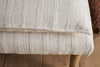 Close-up of the Kiana Cotton Upholstered Bench by nkuku in Natural, featuring beige, textured woven fabric with vertical raised stripes. Resting on visible wooden legs and placed on a wooden floor—an inviting accent for any space.