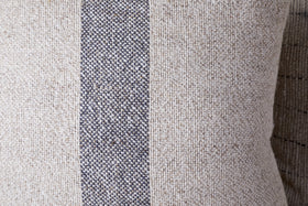 A close-up of the nkuku Kallu Wool & Cotton Cushion Cover - Natural, featuring a visible coarse weave and a vertical dark gray stripe running down the center.