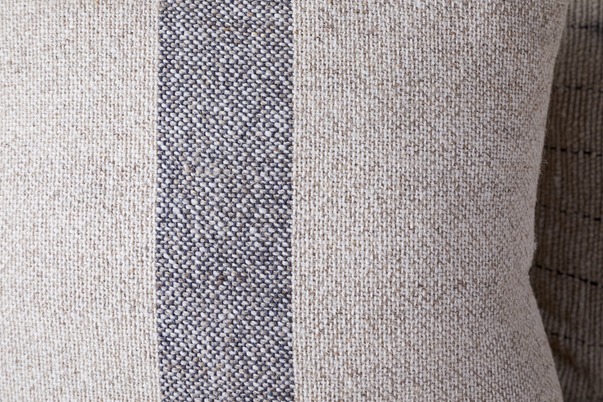 A close-up of the nkuku Kallu Wool & Cotton Cushion Cover - Natural, featuring a visible coarse weave and a vertical dark gray stripe running down the center.
