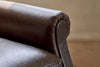 Close-up of the Knada Leather Armchair by nkuku in chocolate brown, focusing on the armrest and seat cushion with soft lighting and a neutral background.