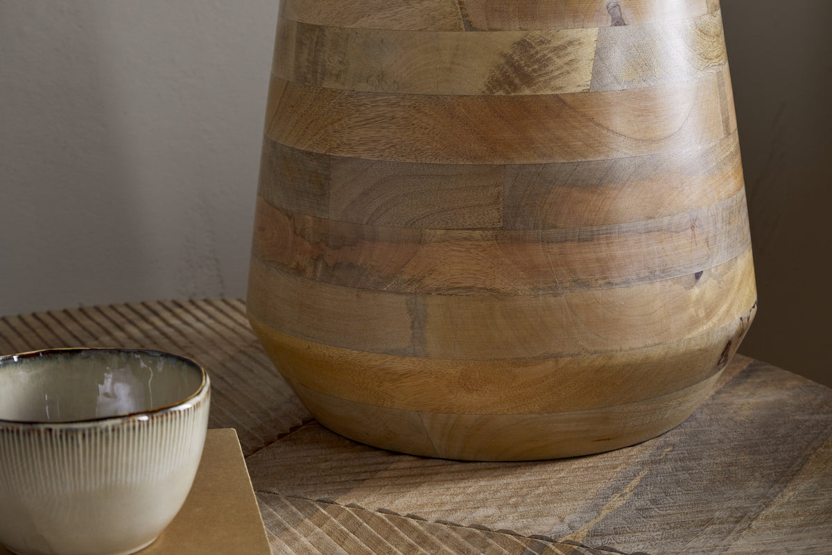 A close-up of the nkuku Kayo Statement Table Lamp, crafted from natural mango wood with visible grain, sits on a wooden table next to a ceramic bowl featuring a white interior and brown rim.