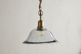 The Keju Organic Shape Recycled Glass Pendant in clear by nkuku features a stylish glass shade suspended from a chain, bringing elegant flair to any room.