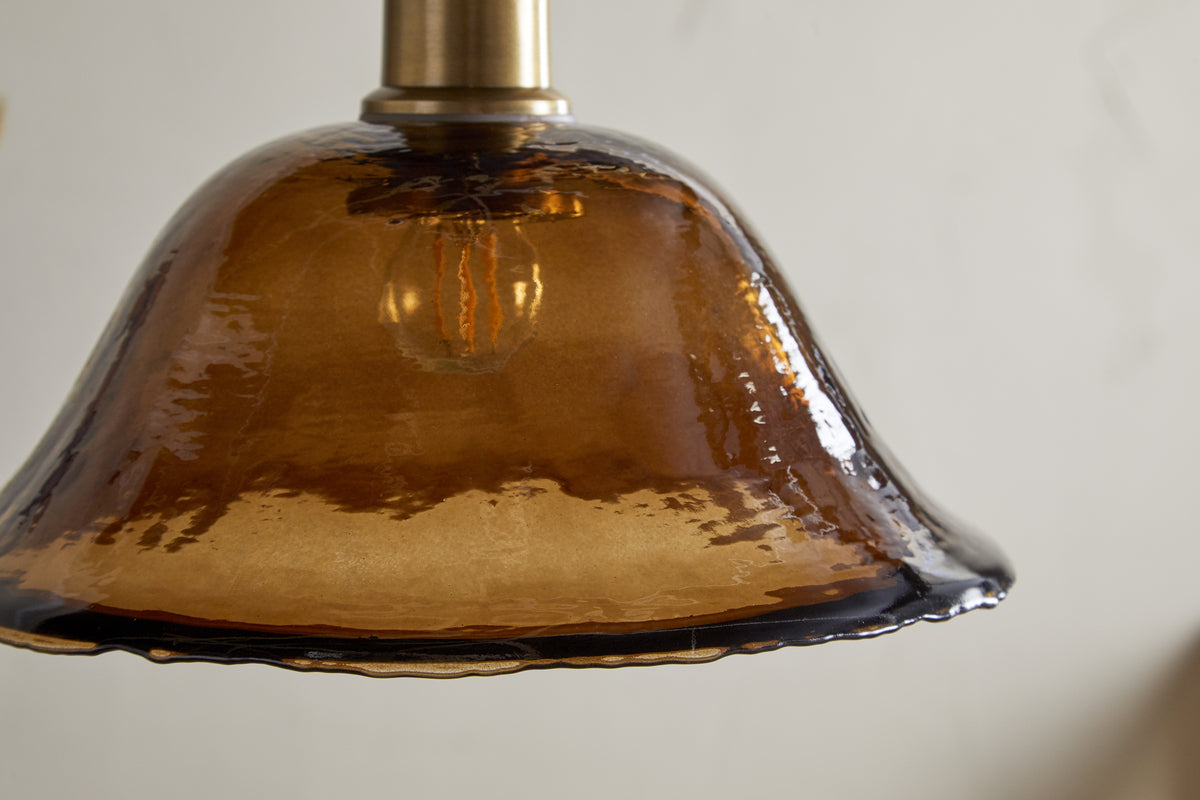 Close-up of the nkuku Keju Organic Shape Recycled Glass Pendant in Dark Amber, showcasing its textured, translucent shade and antique brass fixture against a plain light background.