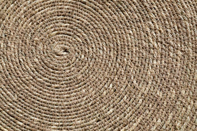 Close-up of the nkuku Keso Woven Placemats - Brown (Set of 4) reveals detailed circular and spiral patterns in natural fibers—perfect as a textured, handcrafted backdrop for minimalist tableware or handwoven coasters.