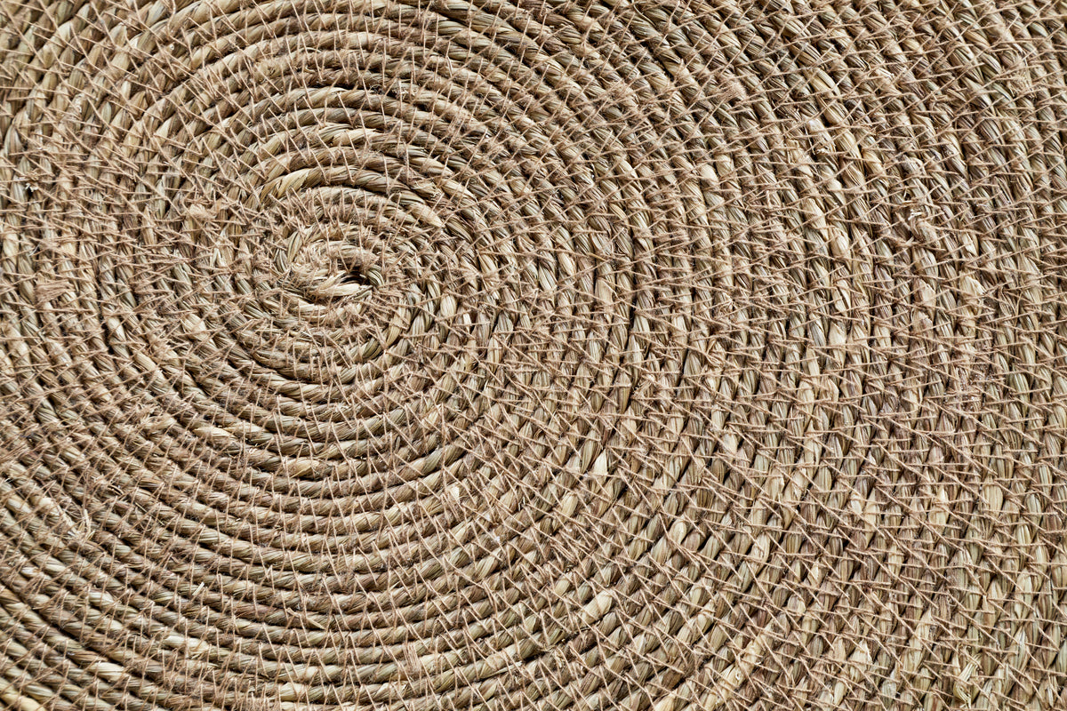 Close-up of the nkuku Keso Woven Placemats - Brown (Set of 4) reveals detailed circular and spiral patterns in natural fibers—perfect as a textured, handcrafted backdrop for minimalist tableware or handwoven coasters.