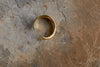 The Katai Ring - Gold by nkuku, featuring a gold-coloured open spiral design, rests on a textured stone surface with dry grass in the lower right corner.