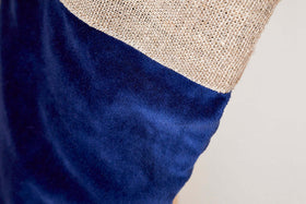 A close-up of the Karru Cotton Velvet Stocking - Indigo by nkuku shows rough, tan burlap-like fabric above smooth indigo cotton velvet, separated by a diagonal seam—ideal for festive fireplace décor or stocking detail.