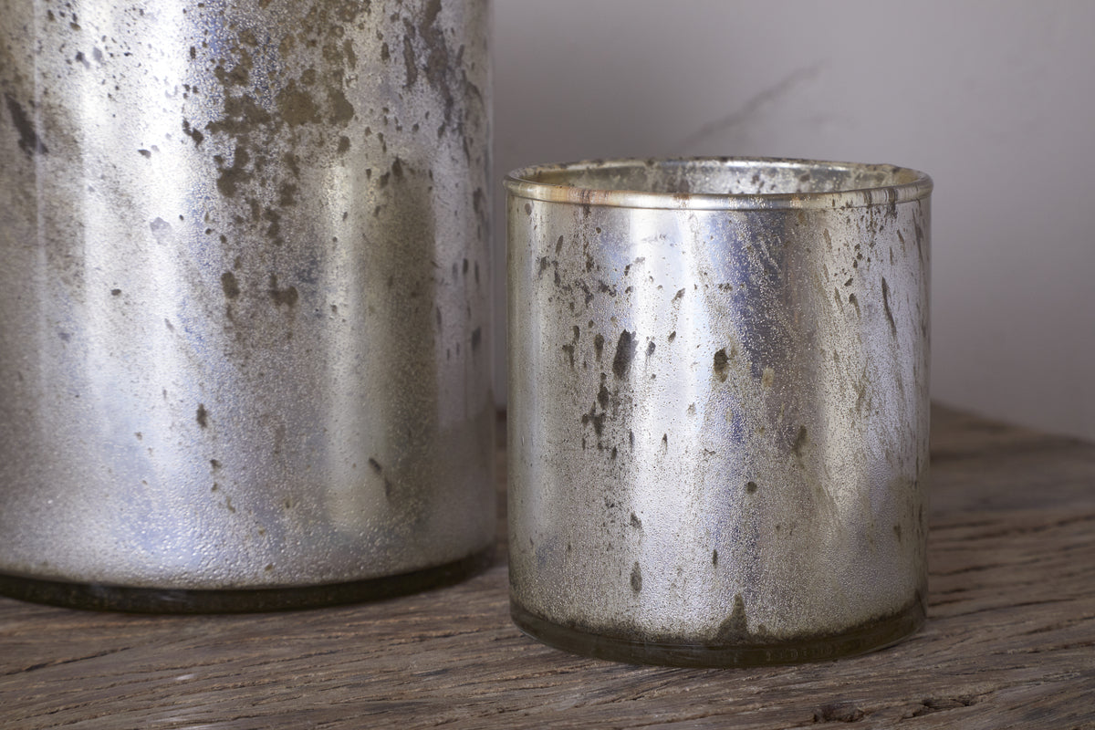 Two rustic gold Kunjari Tealight Holders by nkuku, one large and one small, rest on a wooden surface; the smaller holder sits fully in front—ideal accents for tealights and adding rustic charm.
