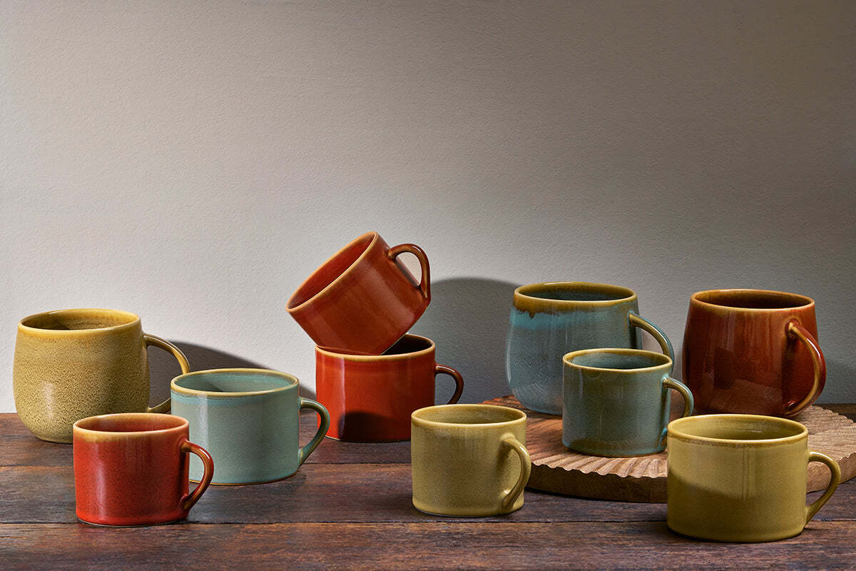 A set of two small nkuku Kalini Mugs in green, kiln-fired and displayed on a rustic wooden surface with a soft gray background.